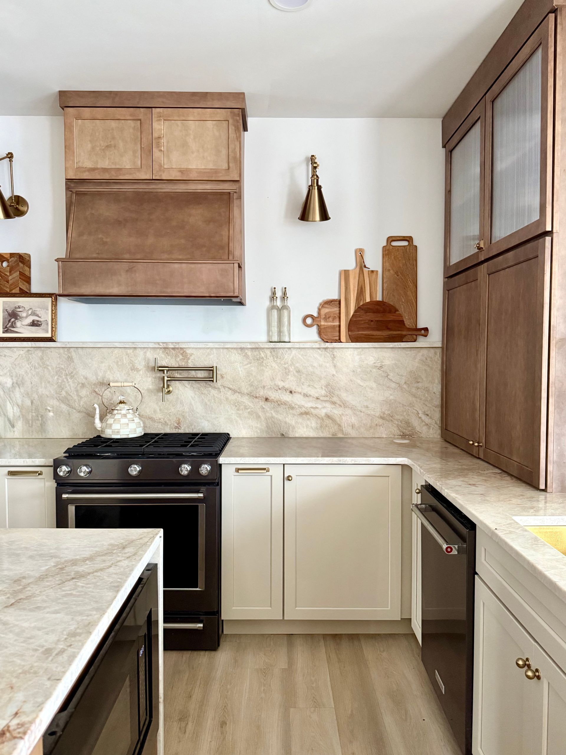 Bright kitchen with white cabinets, wood accents, black stove, and marble-look counters