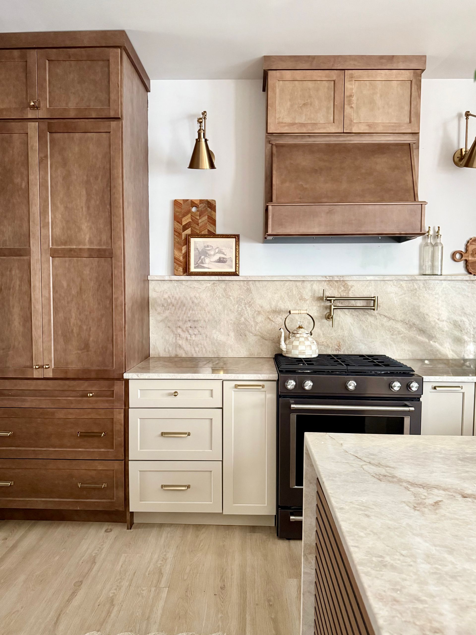 Modern kitchen with wood cabinets, white lower cabinets, marble backsplash, and a stainless gas range.