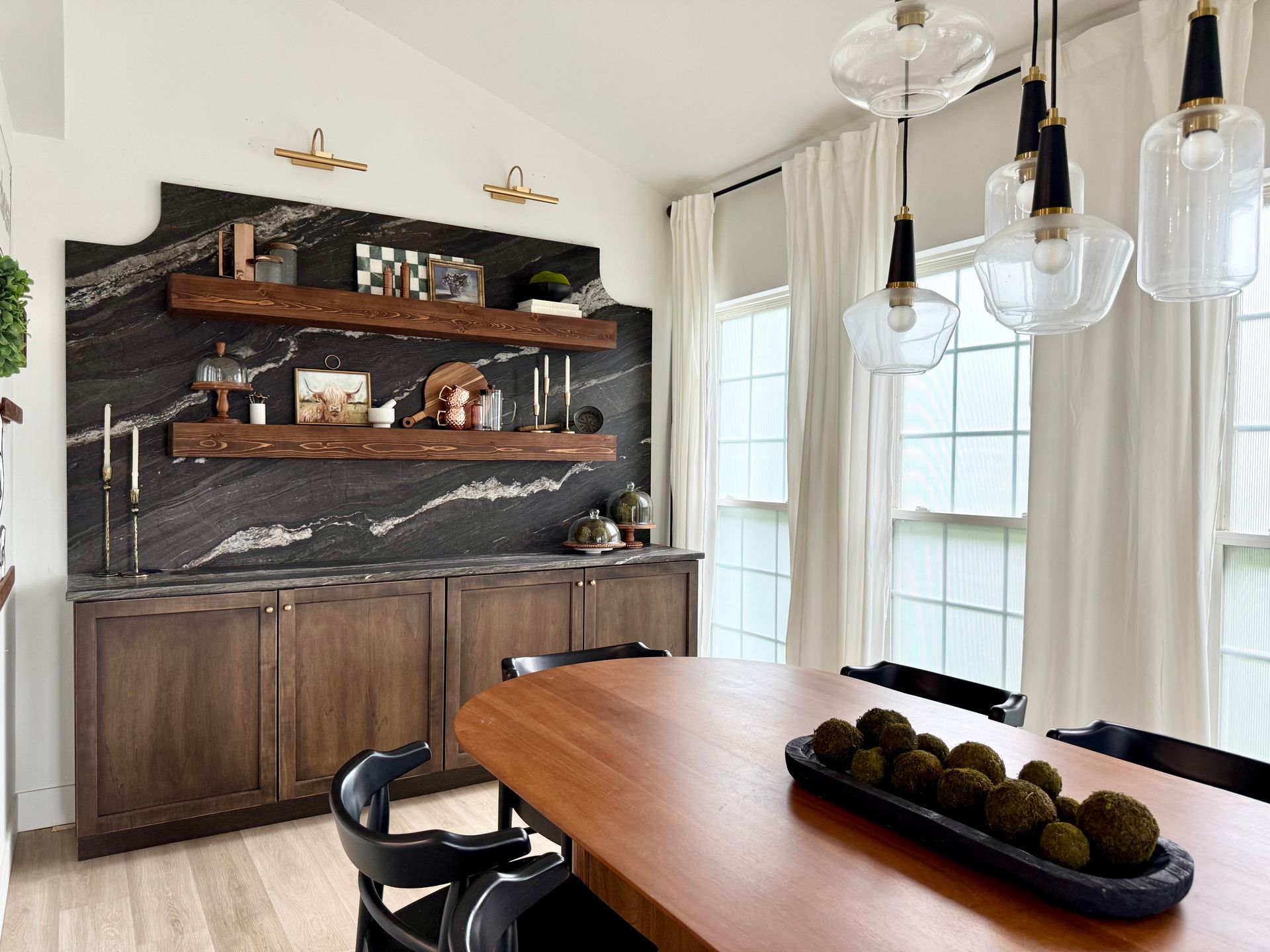 Modern dining room with wood table, black chairs, marble shelves, and pendant lights by tall windows