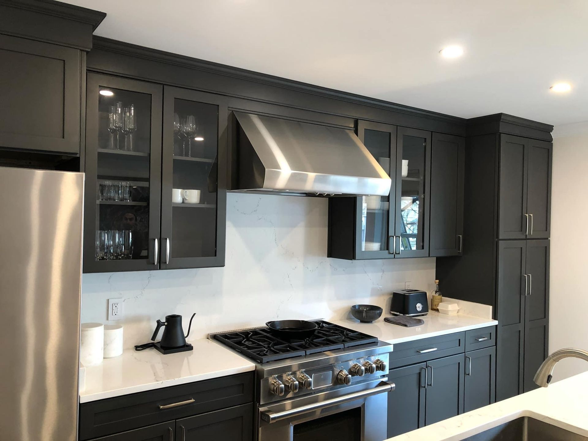 Modern kitchen with dark cabinets, stainless steel appliances, white countertops, and a stainless range hood
