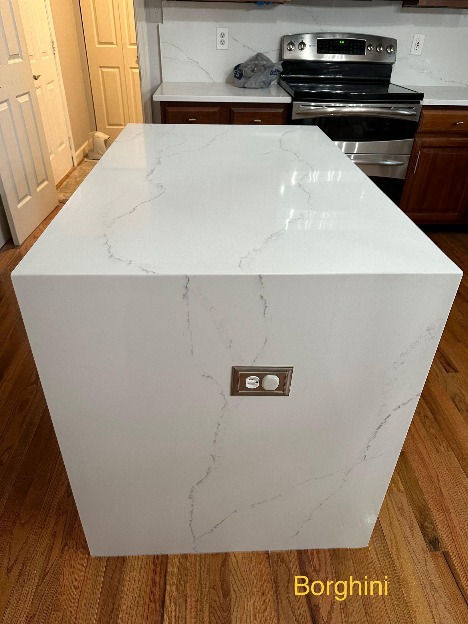 White marble kitchen island with a built-in outlet, in front of a stove and cabinets.