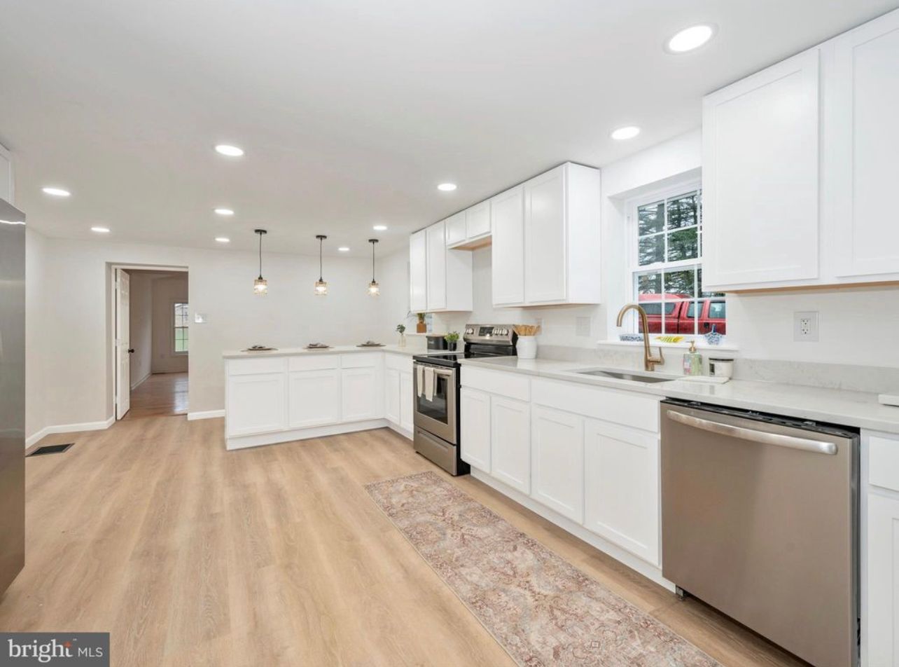 Bright modern white kitchen with island, stainless appliances, pendant lights, and light wood floors