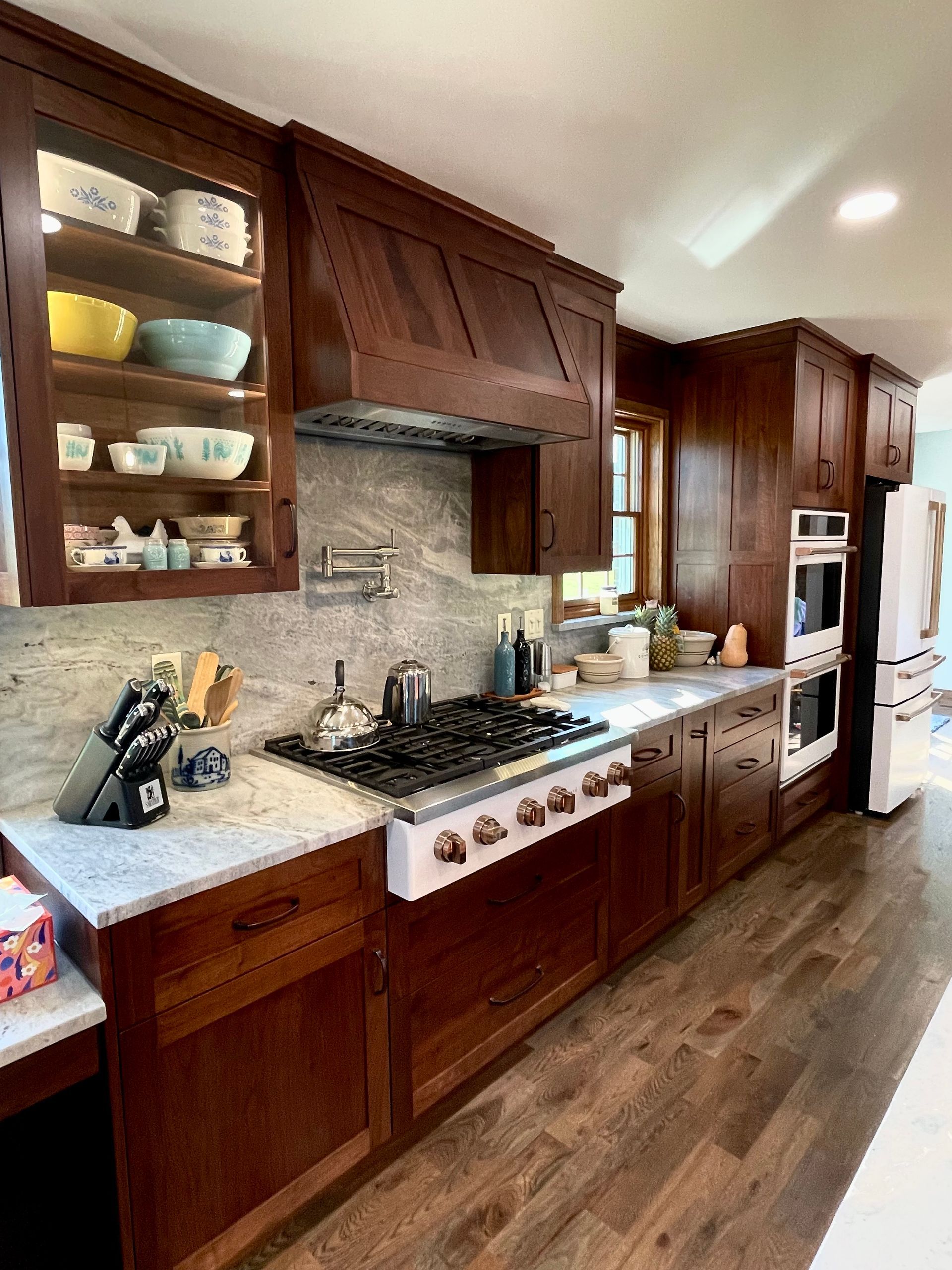 Wood-paneled kitchen with white countertops, gas range, open shelves, and stainless steel refrigerator.
