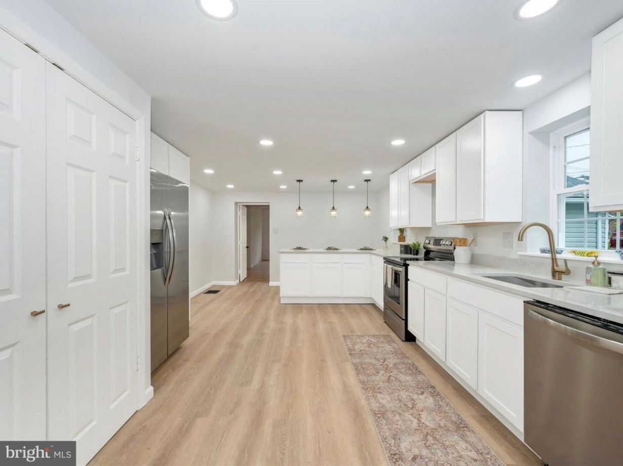 Bright modern white kitchen with stainless appliances, wood floors, and a narrow runner rug