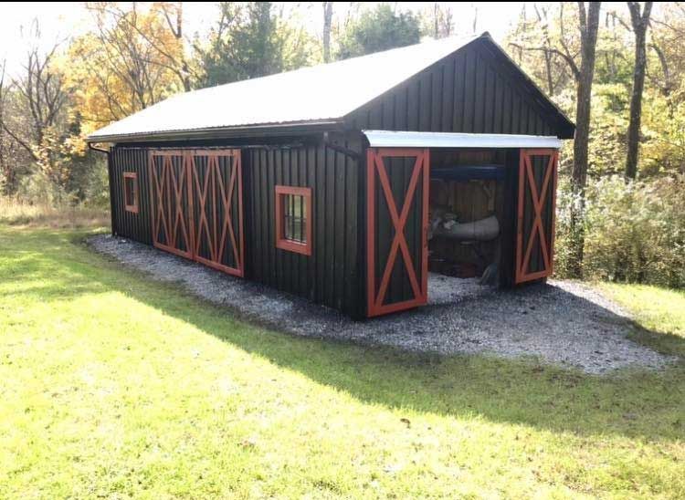 A black barn with red doors is sitting in the middle of a grassy field.