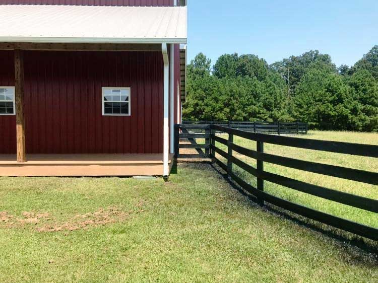 A barn with a porch and a black fence in front of it.