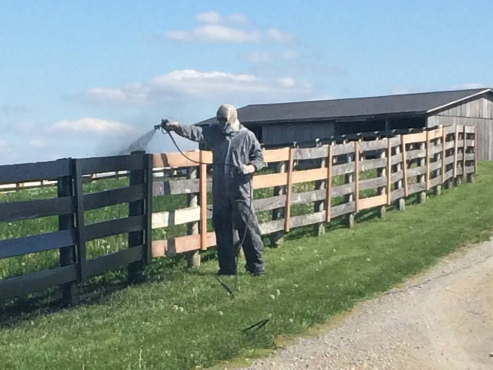 A man spraying a wooden fence with a sprayer