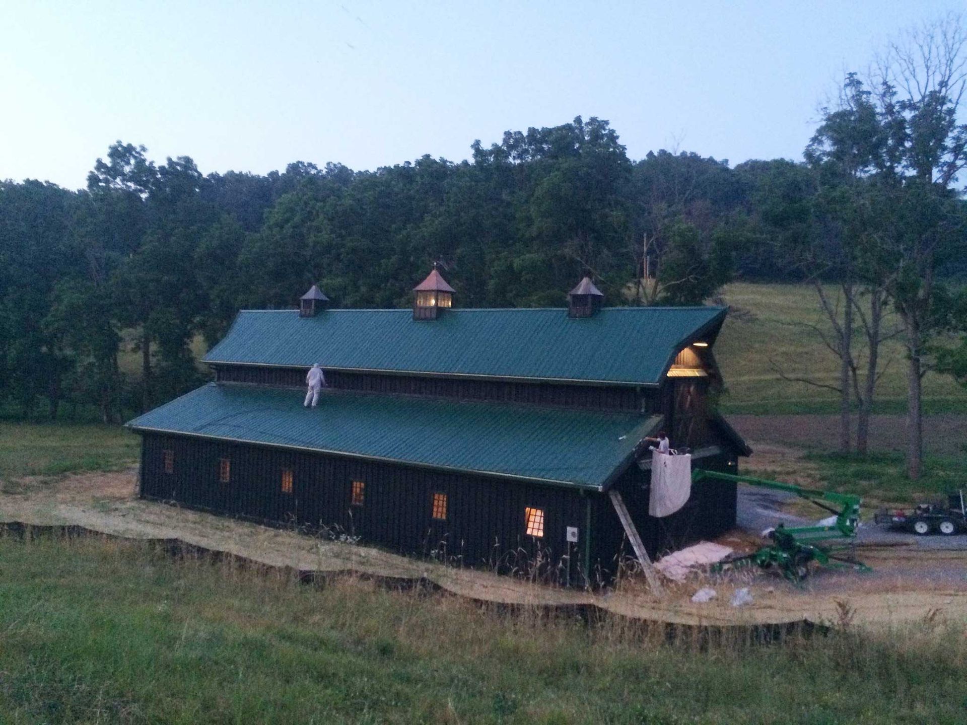 A large barn with a green roof is sitting in the middle of a field.
