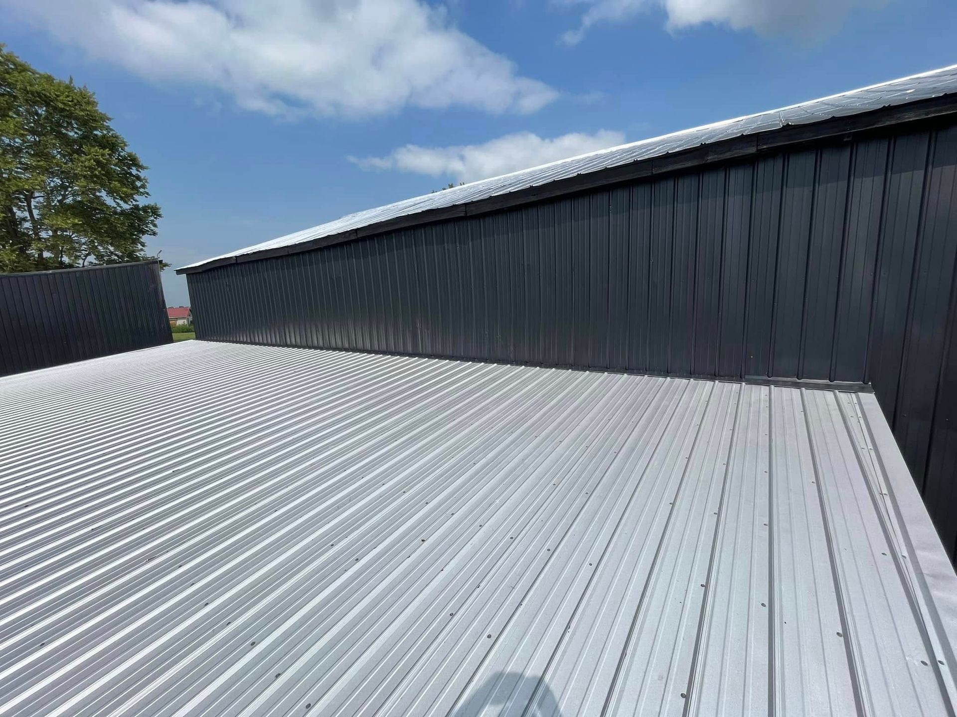 Ribbed silver metal roof beside a black building under a blue sky with clouds