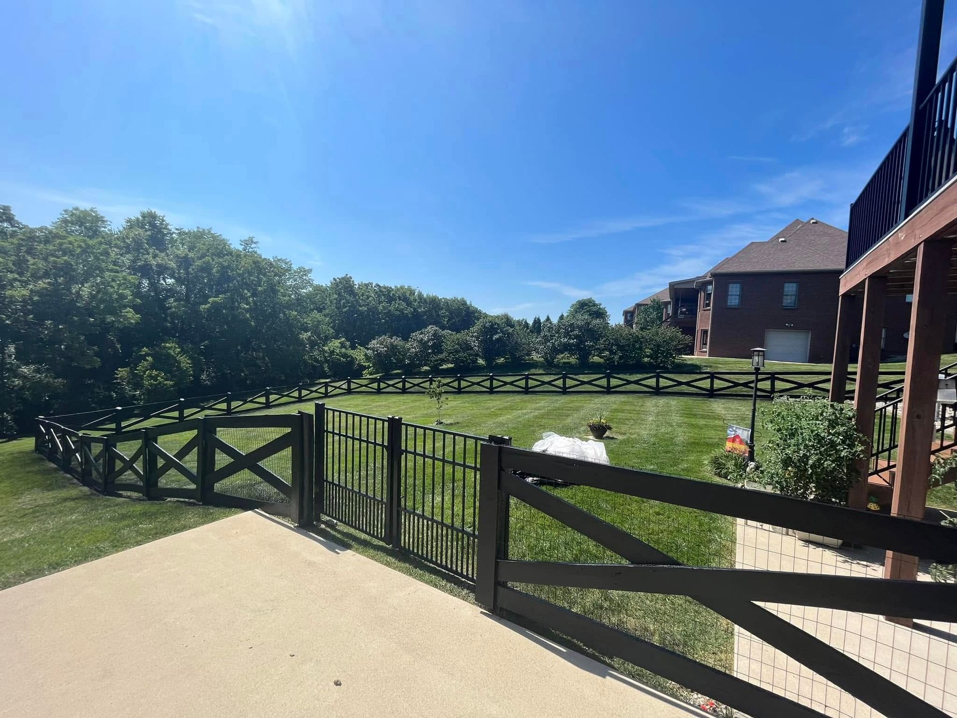 Sunny backyard with black fence, green lawn, white fountain, and brick house under a blue sky