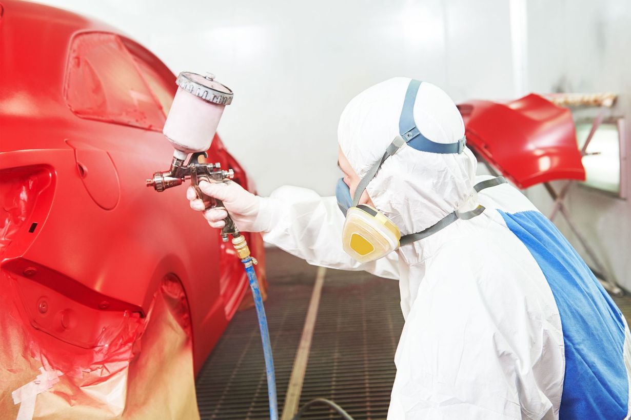 Worker in protective suit spray-painting a red car in a paint booth