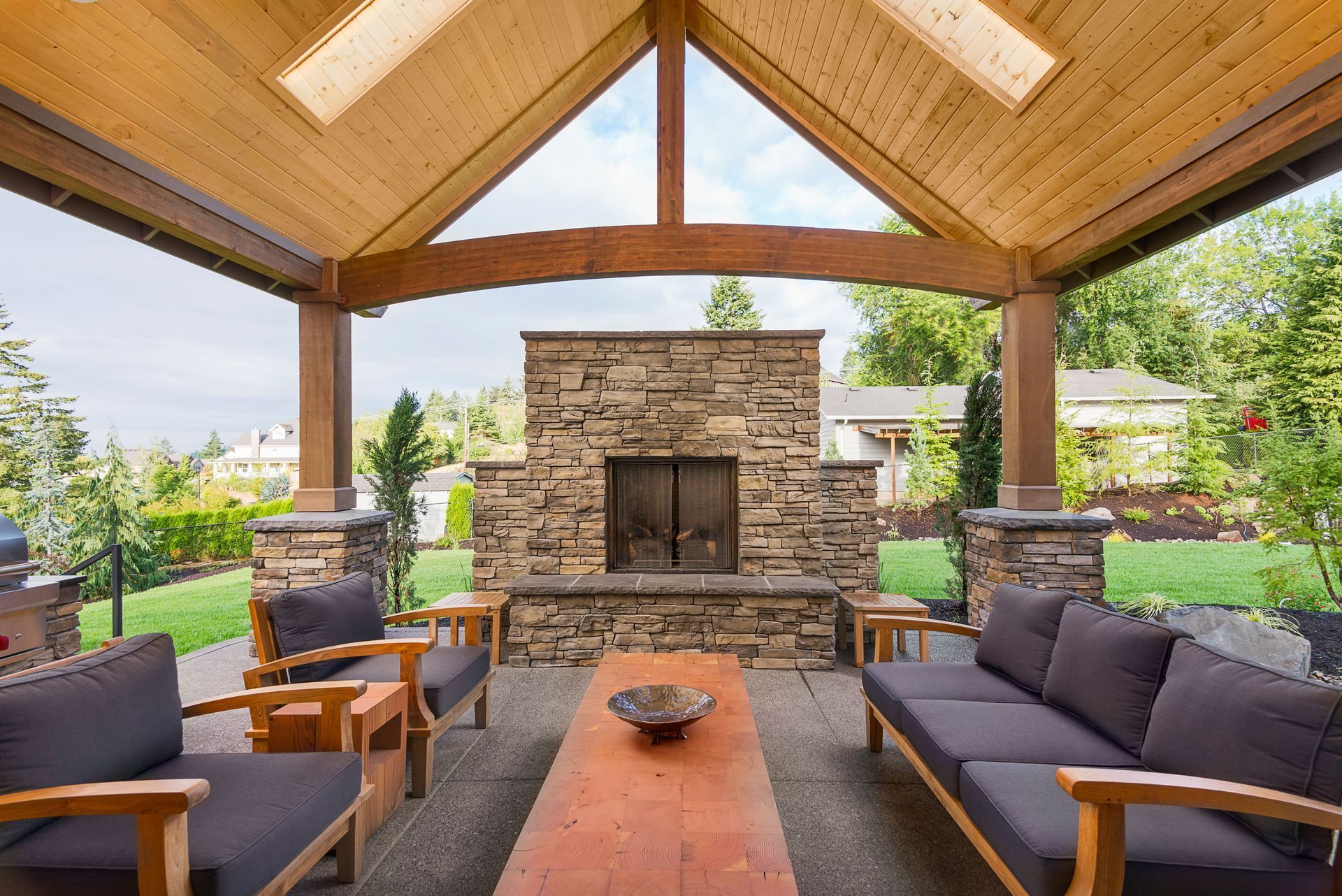 Covered patio with stone fireplace, wooden beams, seating, and a long wooden coffee table.