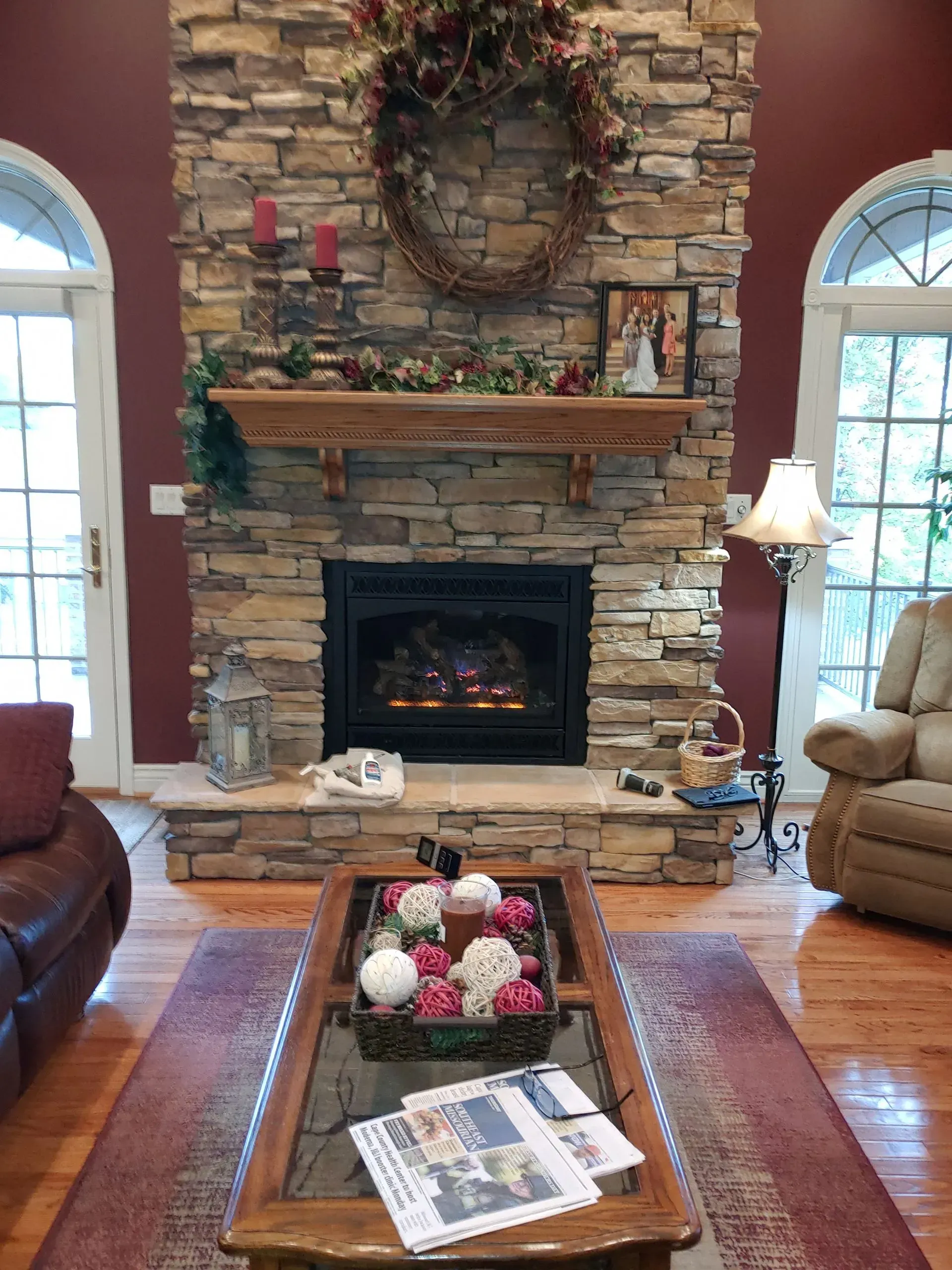 Living room with stone fireplace, wreath, candles, and coffee table with floral arrangement.