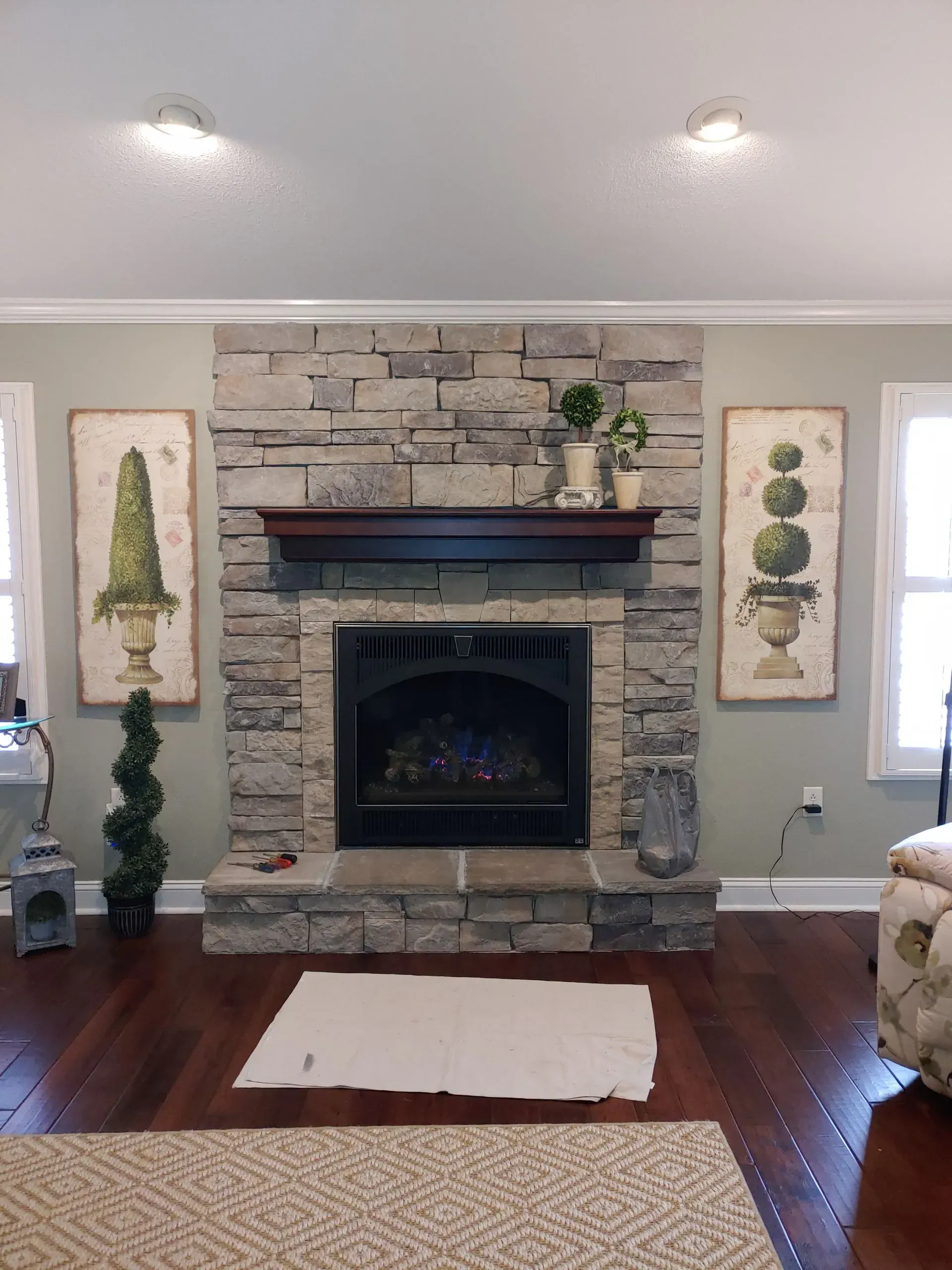 Fireplace with stone surround, dark mantel, flanked by two framed plant prints.