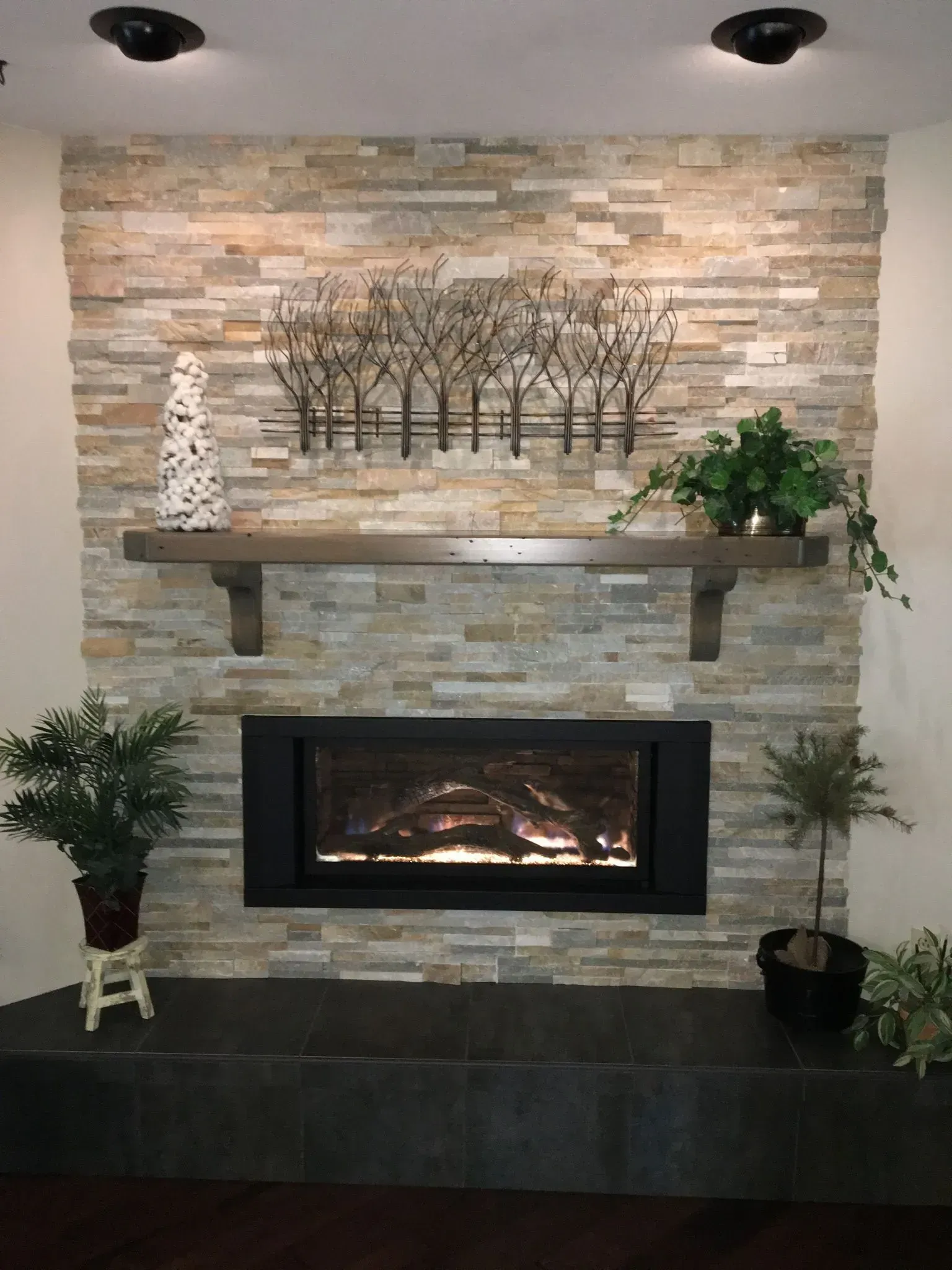 Fireplace with stone accent wall, wooden mantel, and decorative metal tree art.