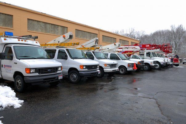 Utility trucks and cherry pickers lined up outside a beige building on a wet, snowy lot.