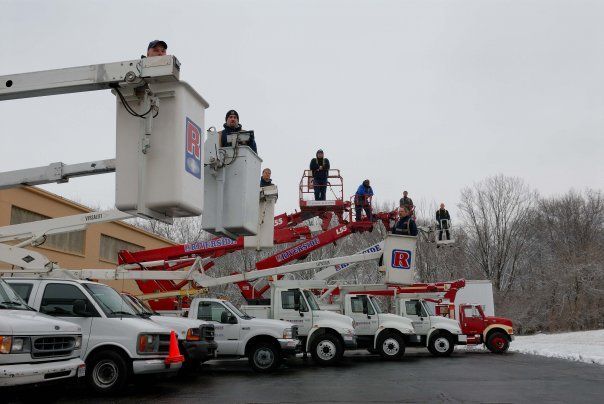 Utility trucks and workers on lift platforms in a snowy roadside scene