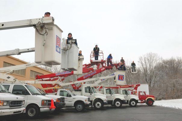 Utility crews on bucket trucks and cherry pickers working on overhead lines in a snowy parking lot