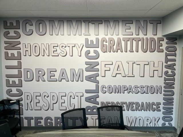 Wall mural with large motivational words like commitment, honesty, faith, and respect above office chairs.