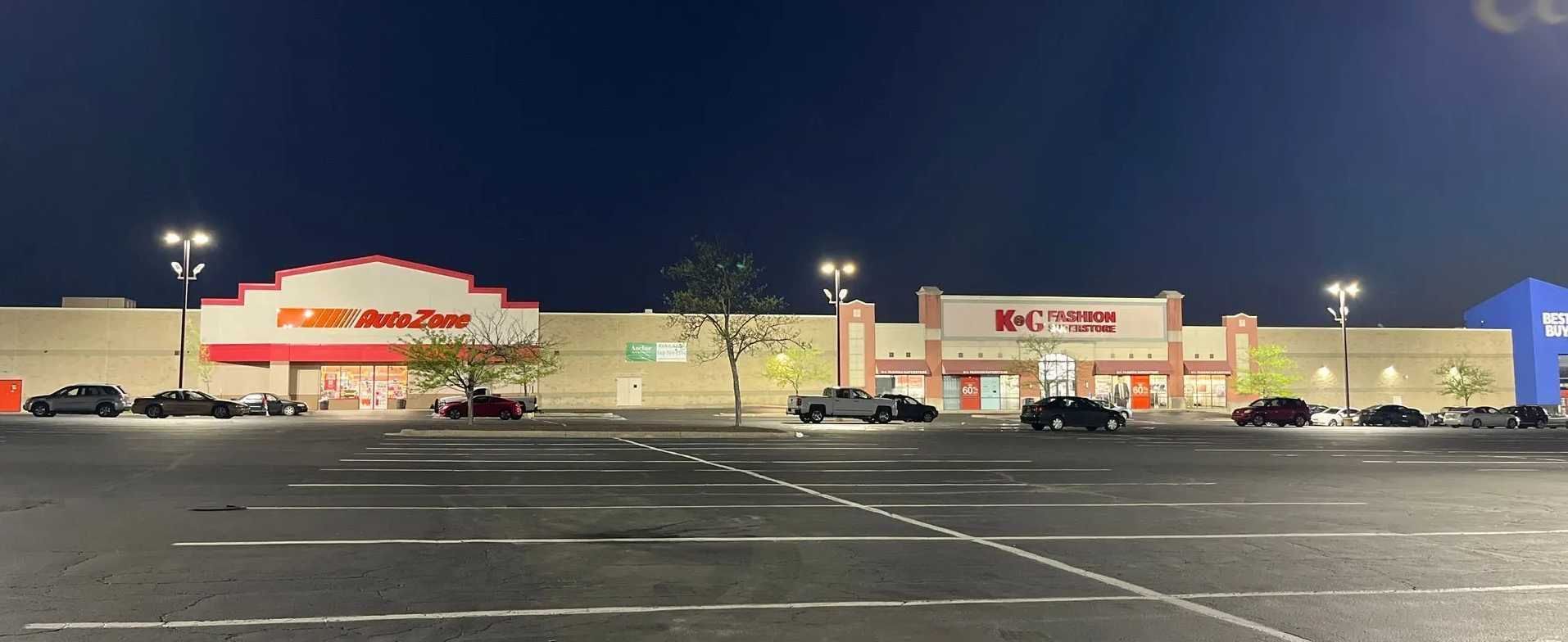Exterior of a strip mall at night with parking lot and several lit businesses.