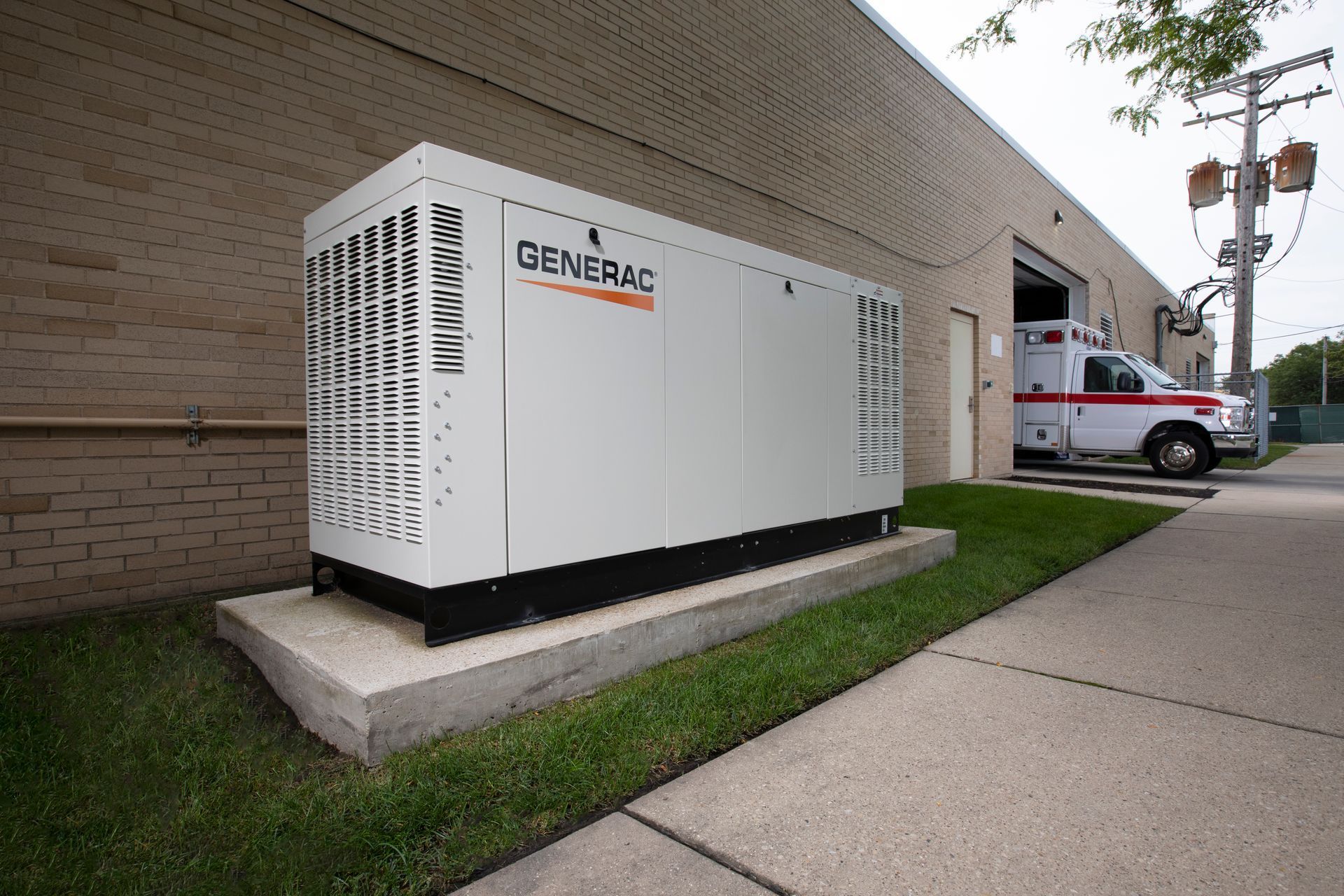 Large white Generac backup generator beside a brick building on a concrete pad near a sidewalk