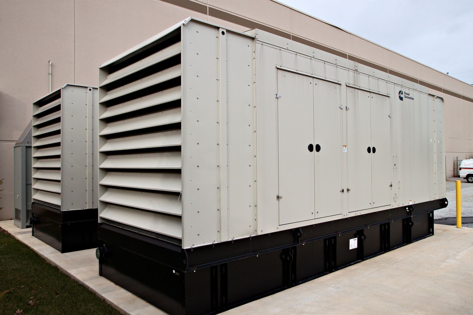 Two large beige industrial generators with black bases sit outside a building.