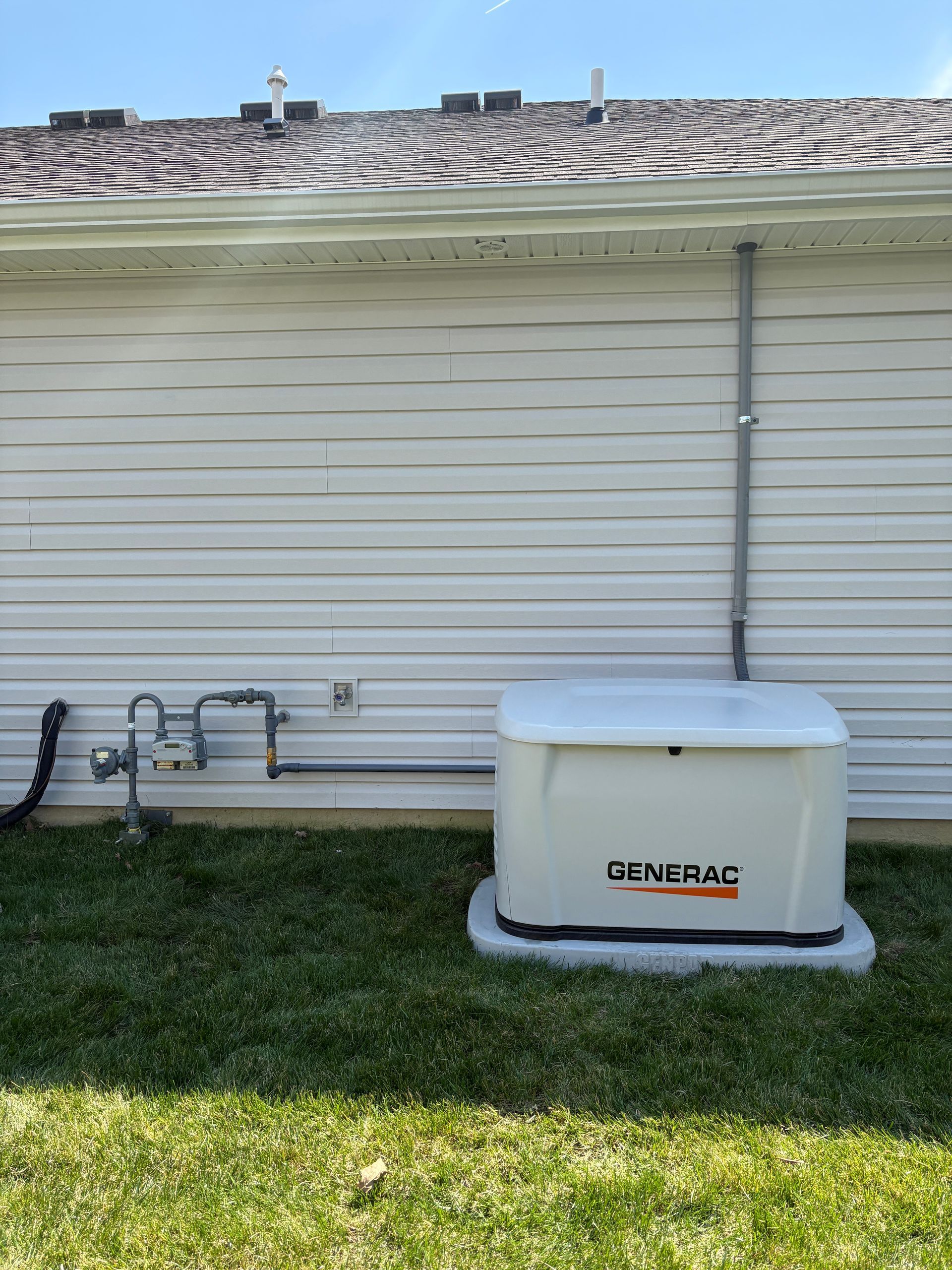 Generator beside house wall on grass, with gray siding and rooftop visible.