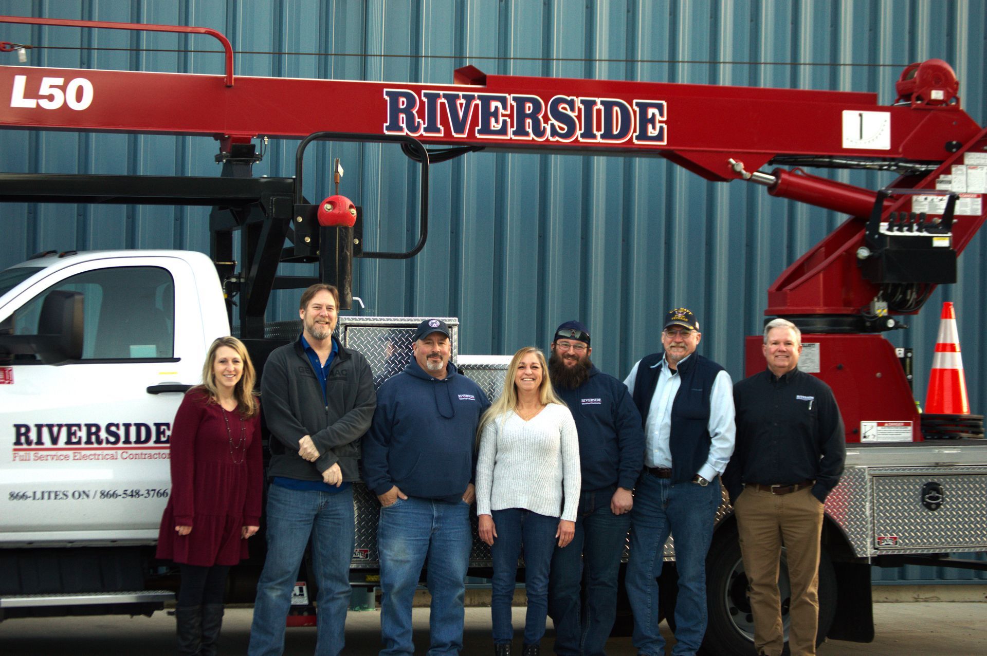 Six people posing in front of a red Riverside crane truck