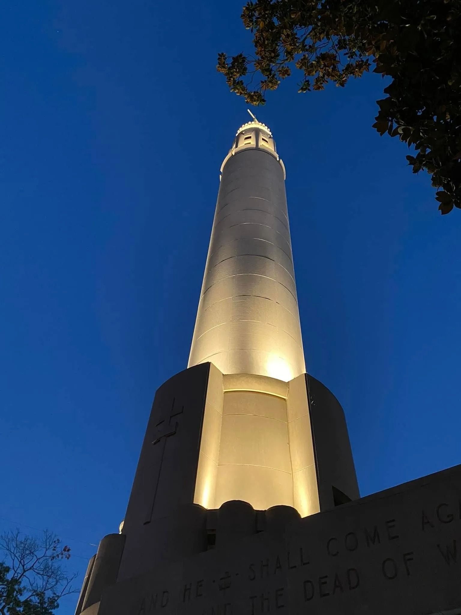 Illuminated tall tower against a deep blue night sky, viewed from below.
