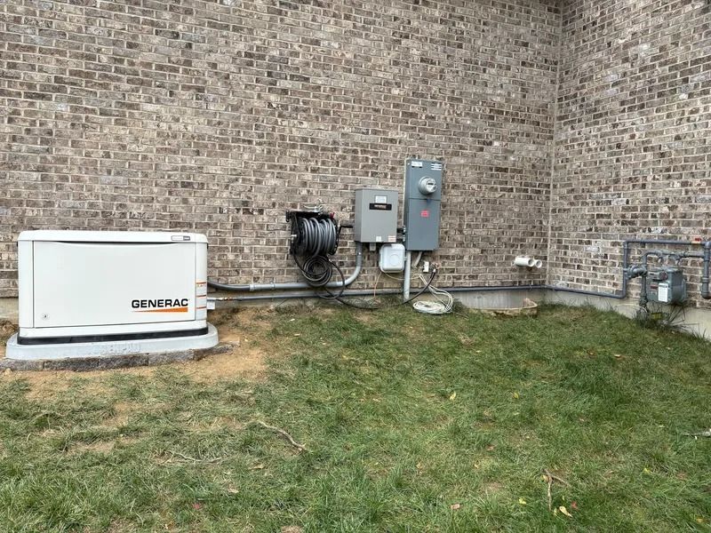 Backyard corner with brick wall, utility panels, and air conditioning unit beside grass