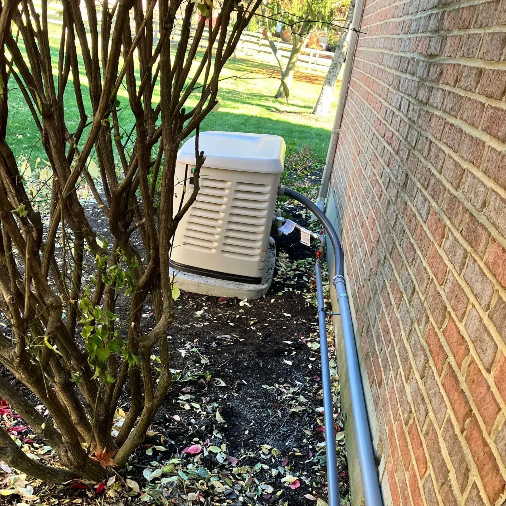 Outdoor HVAC unit beside a brick house, partly hidden by shrubs and a garden bed