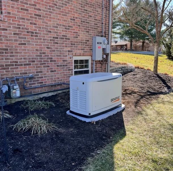 Outdoor backup generator beside a brick house, near an electrical panel, on a grassy yard.