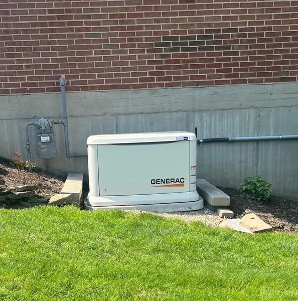 White Generac generator beside a brick house wall on a concrete pad, next to a green lawn.
