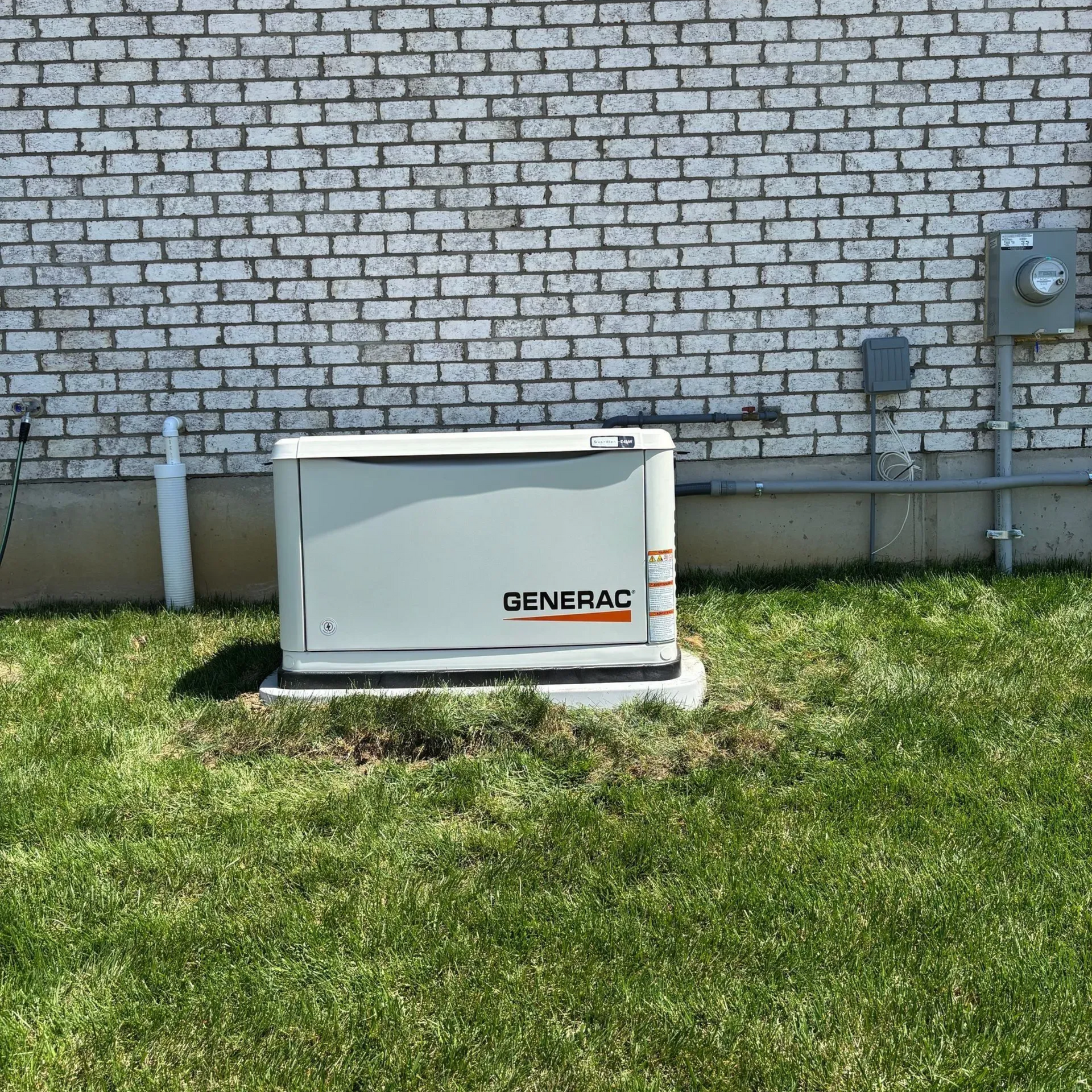 Gray Generac generator on a concrete pad beside a brick wall and grass.