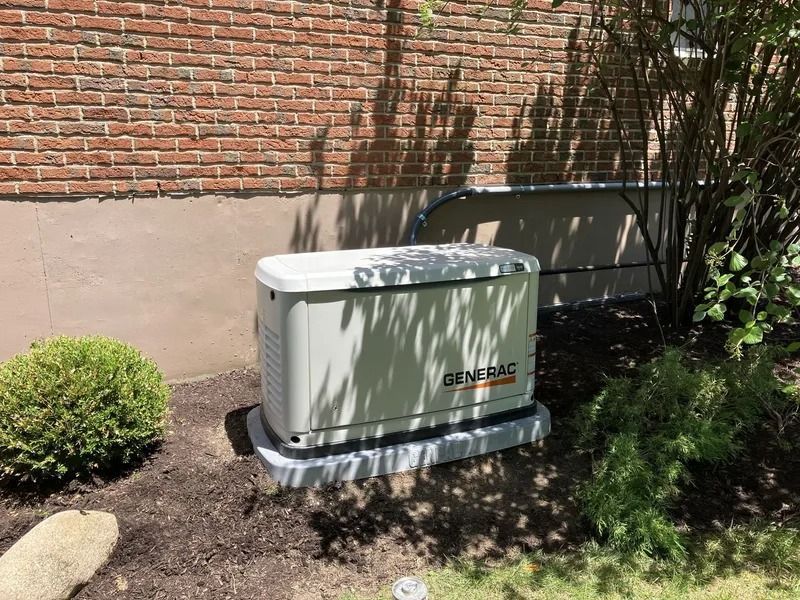 Outdoor generator beside a brick wall and shrubs in a landscaped yard