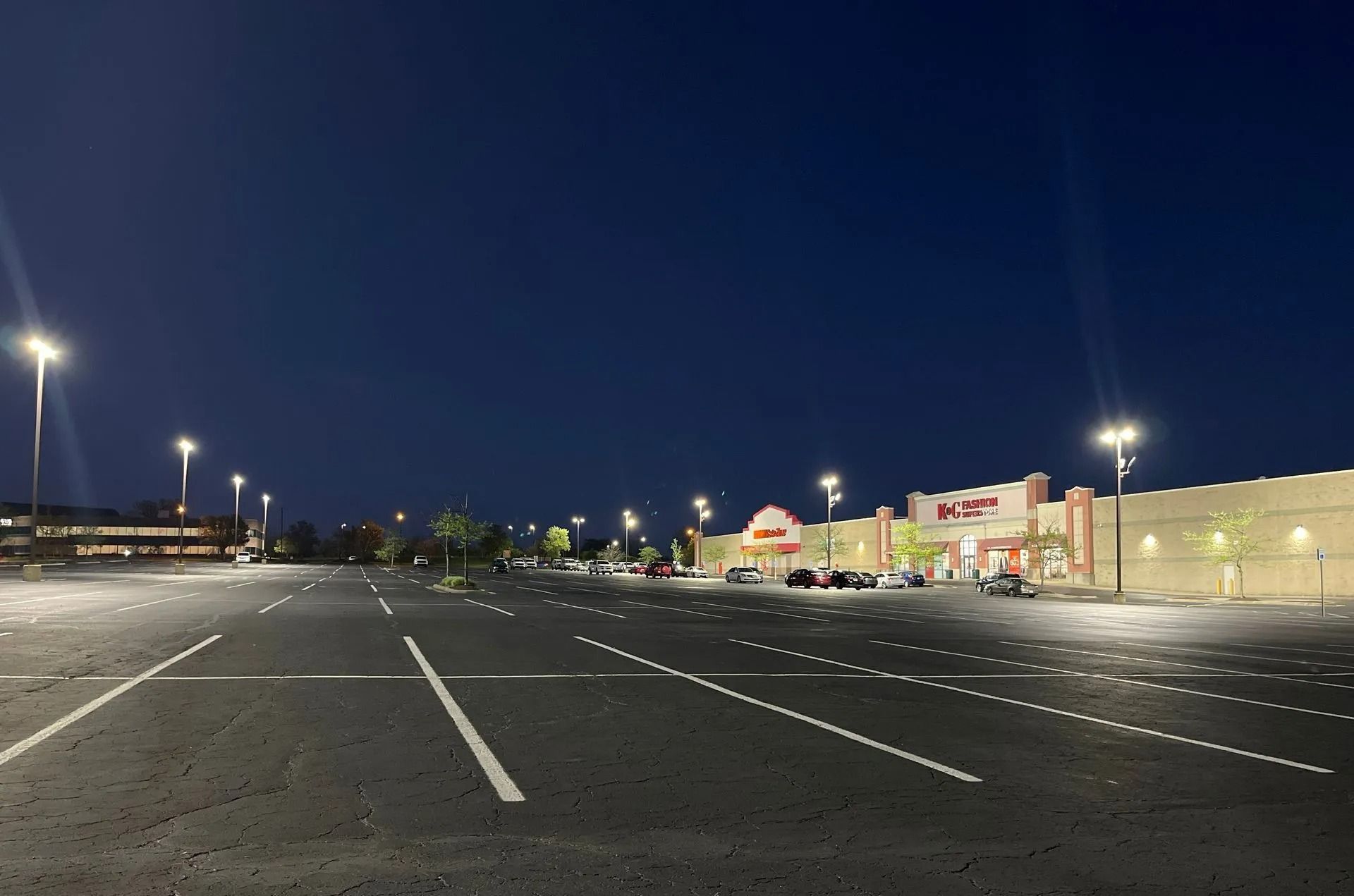 Empty parking lot at night with bright store lights and a deep blue sky