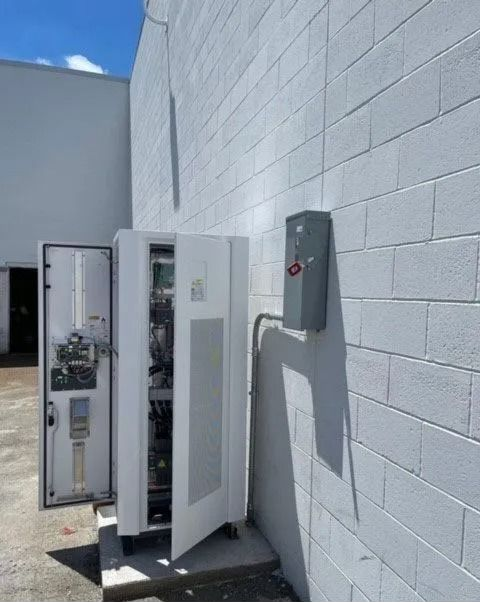 Open electrical cabinets beside a white cinderblock wall outdoors