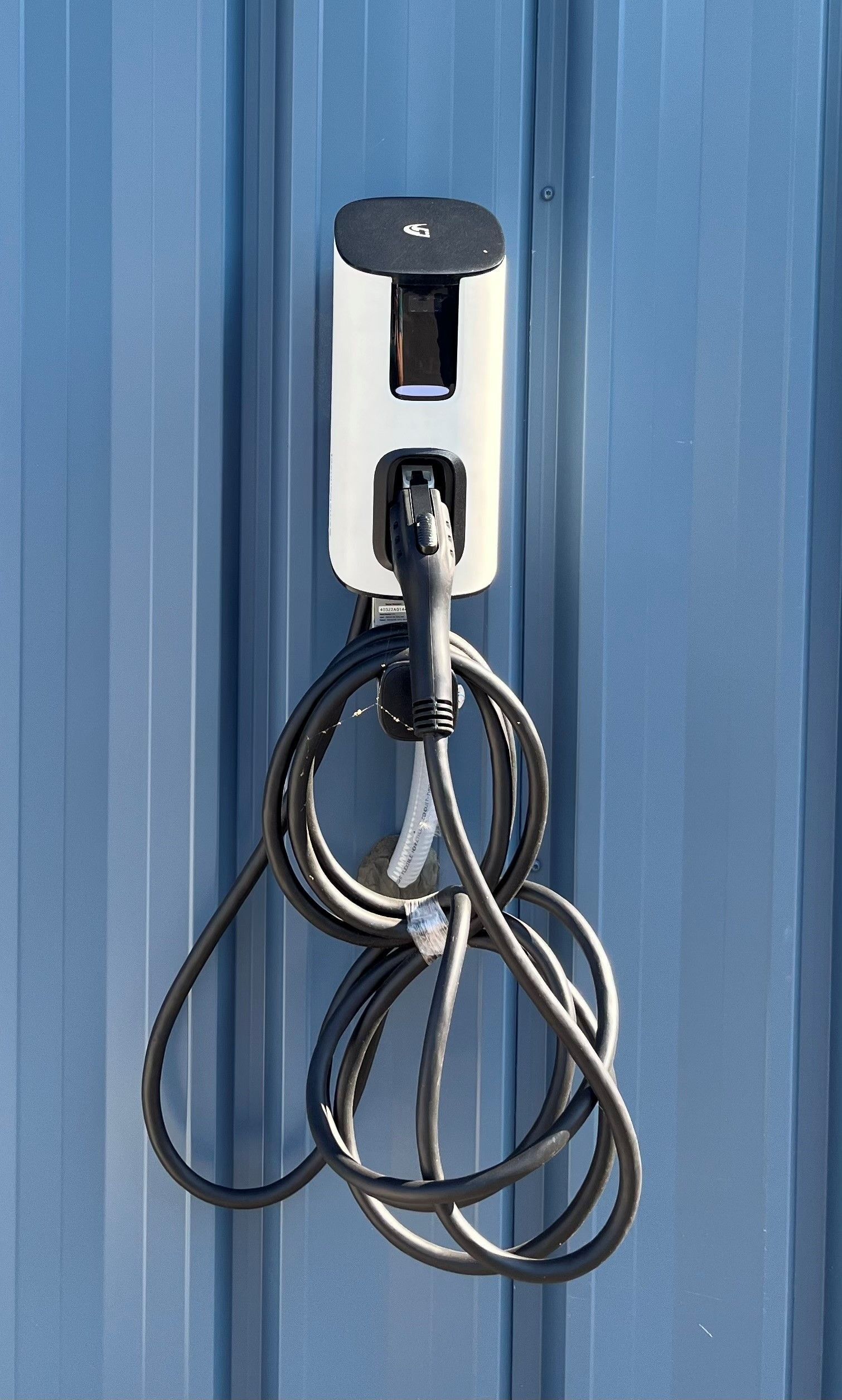 Wall-mounted silver charging dock with black cables hanging against a blue corrugated wall