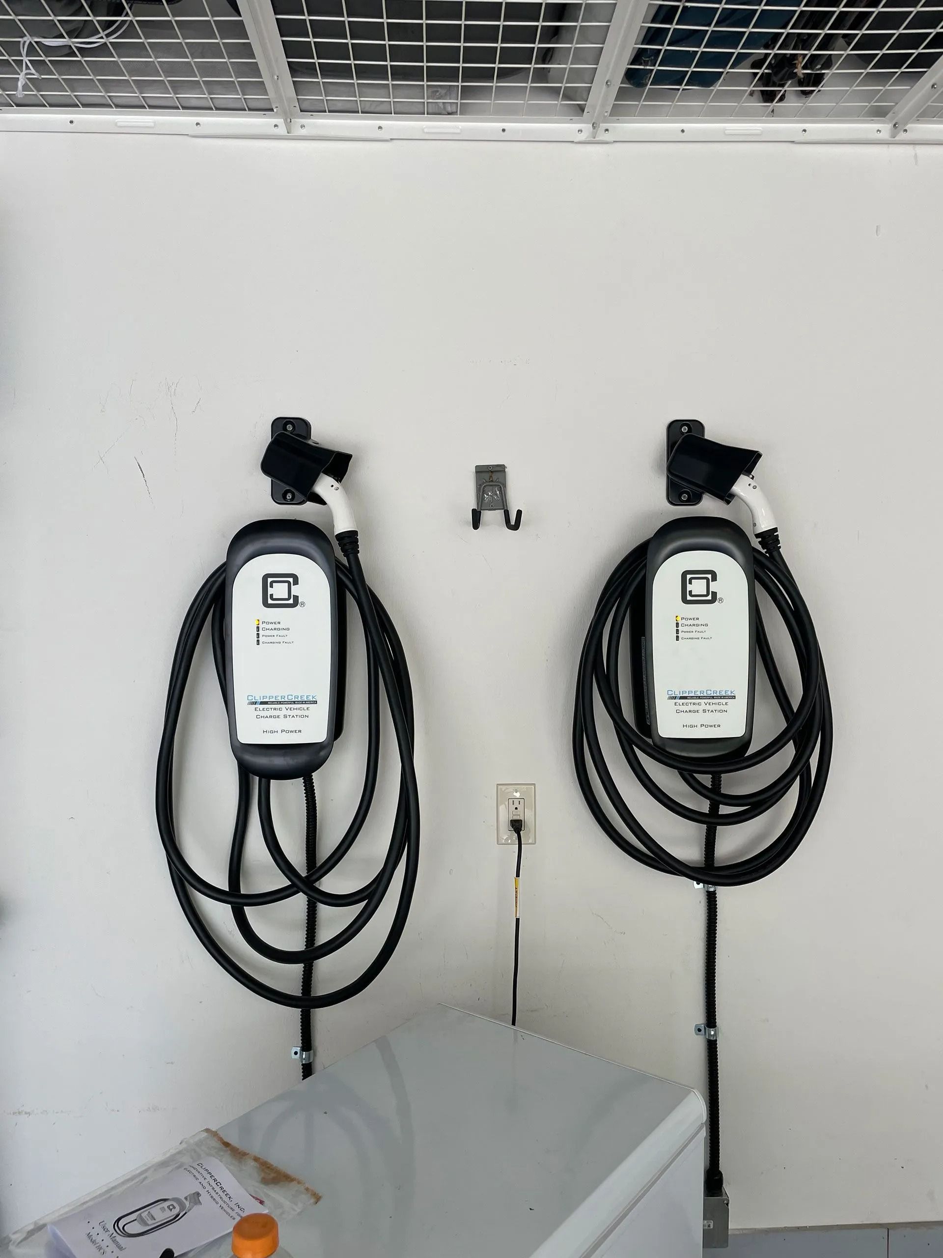Two black wall-mounted EV chargers with coiled cables on a white wall in a garage.