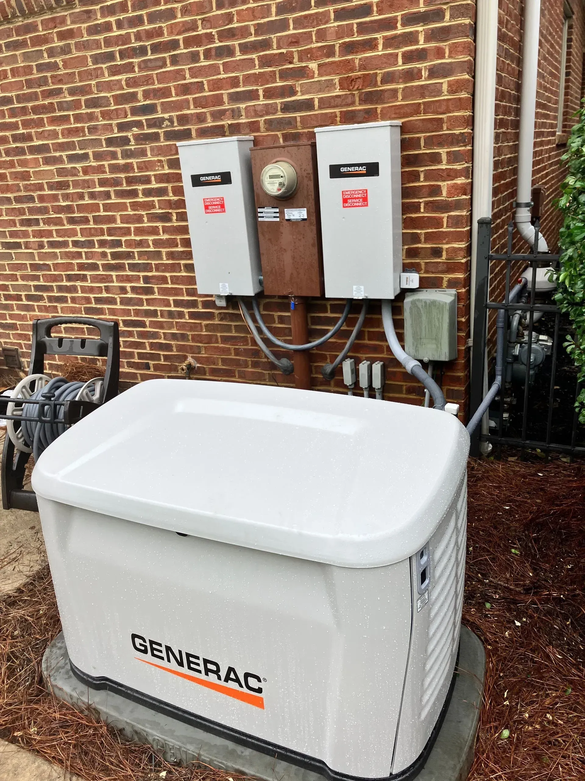 White Generac home generator beside brick wall with electrical panels and conduit.