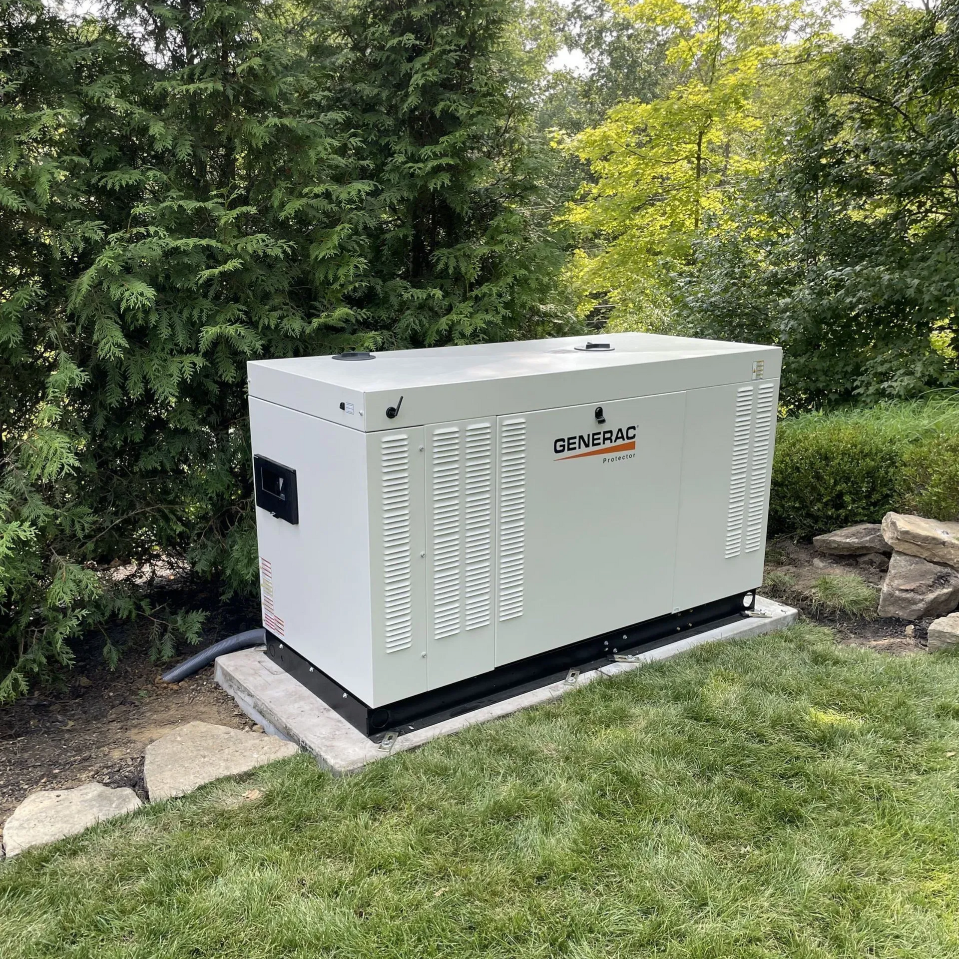 White Generac standby generator on a concrete pad beside a lawn and shrubs