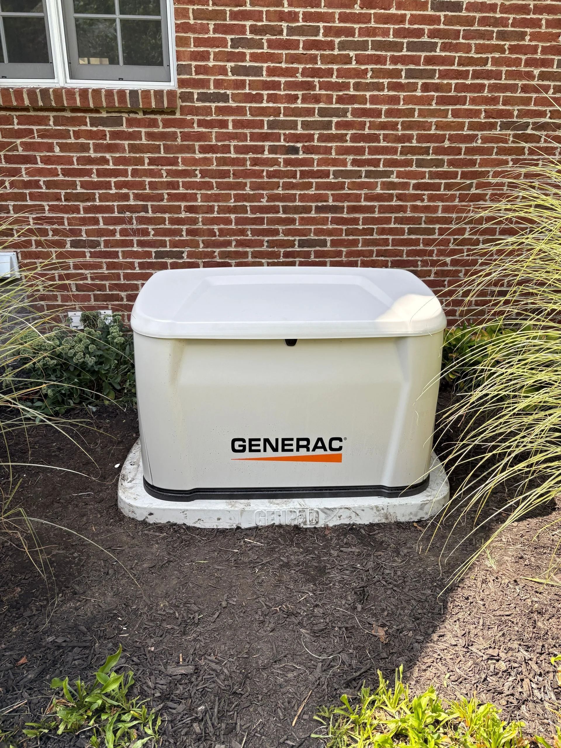 Generac home generator beside a brick house, surrounded by mulch and shrubs