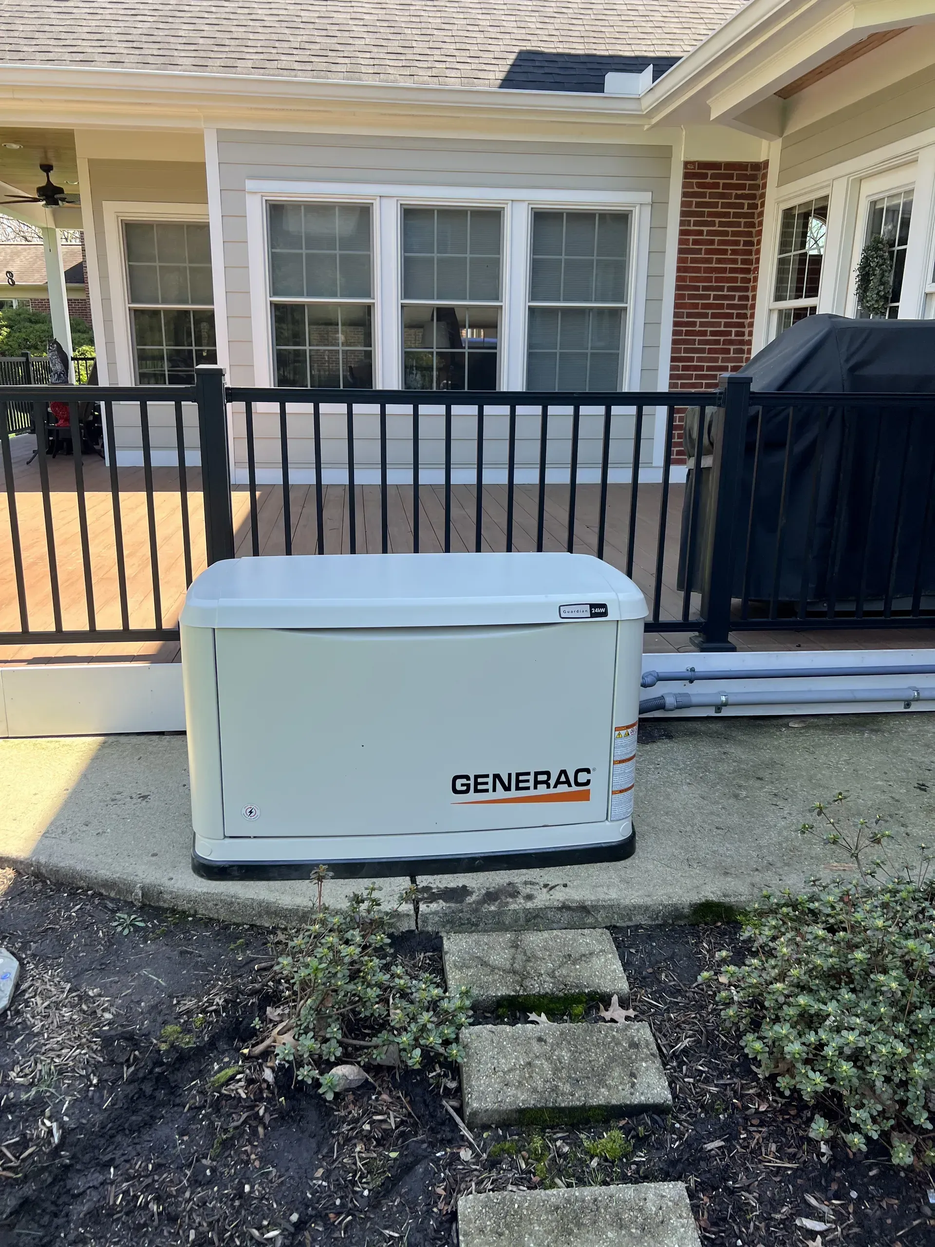 White backup generator beside a black fence in front of a house and window