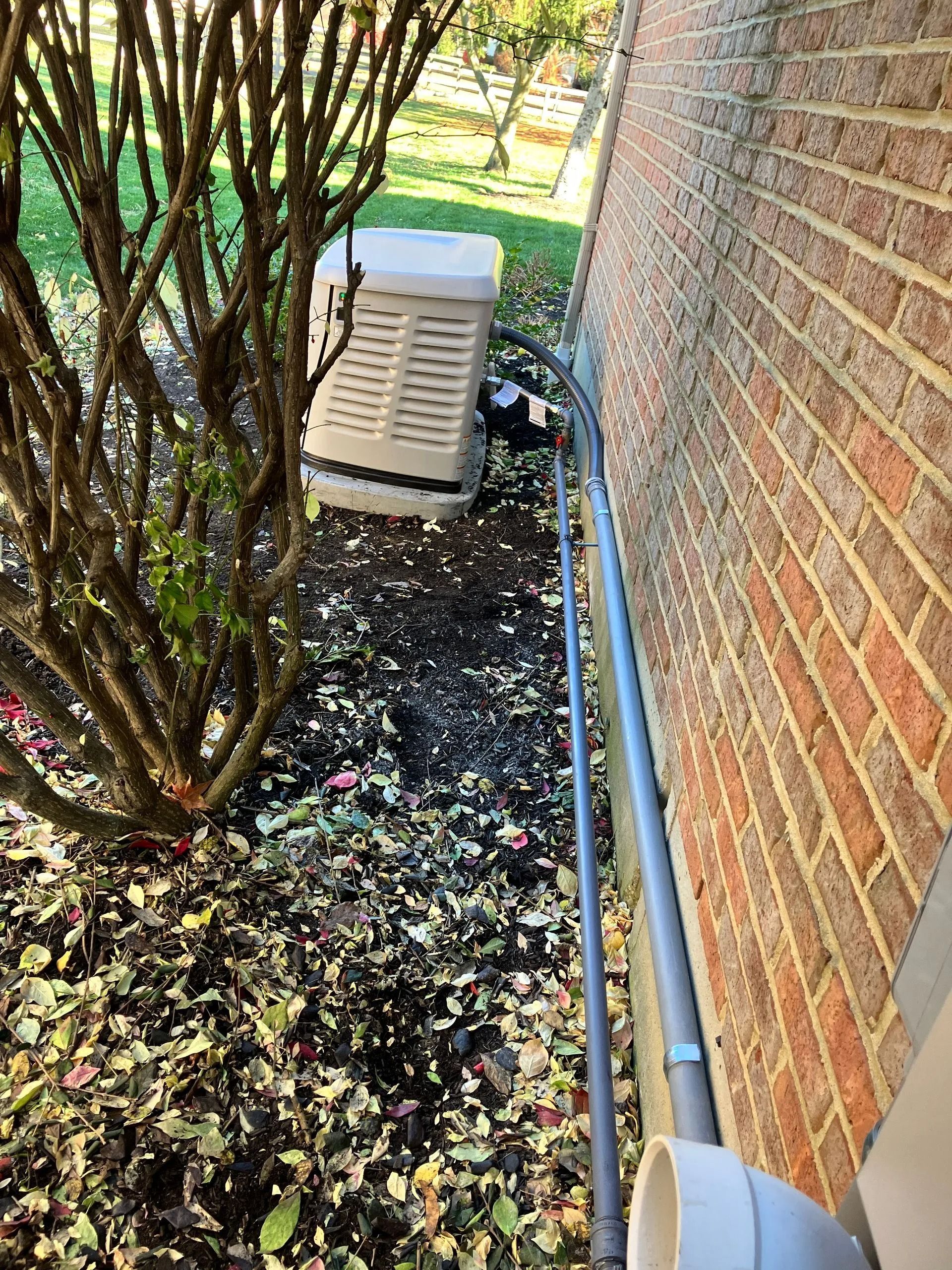 Narrow side yard with brick wall, tree, air conditioner unit, and ground covered in fallen leaves.