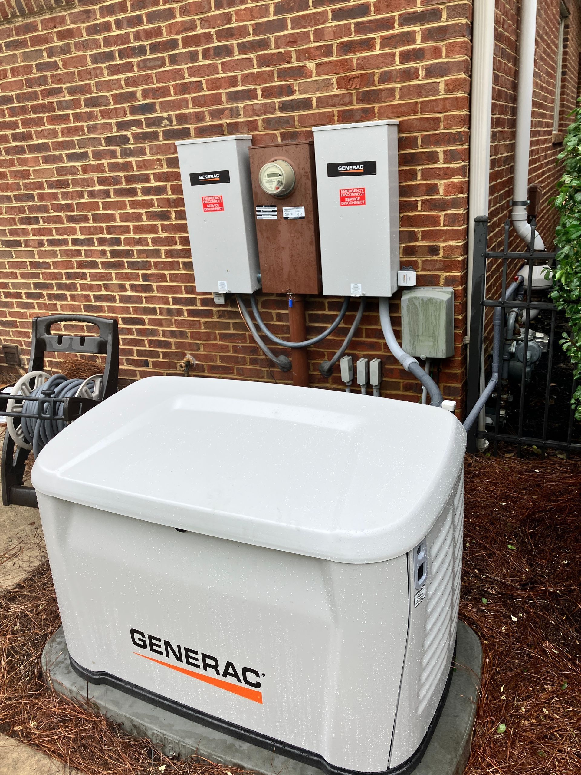 Generac home standby generator beside brick wall with two electrical panels and conduits