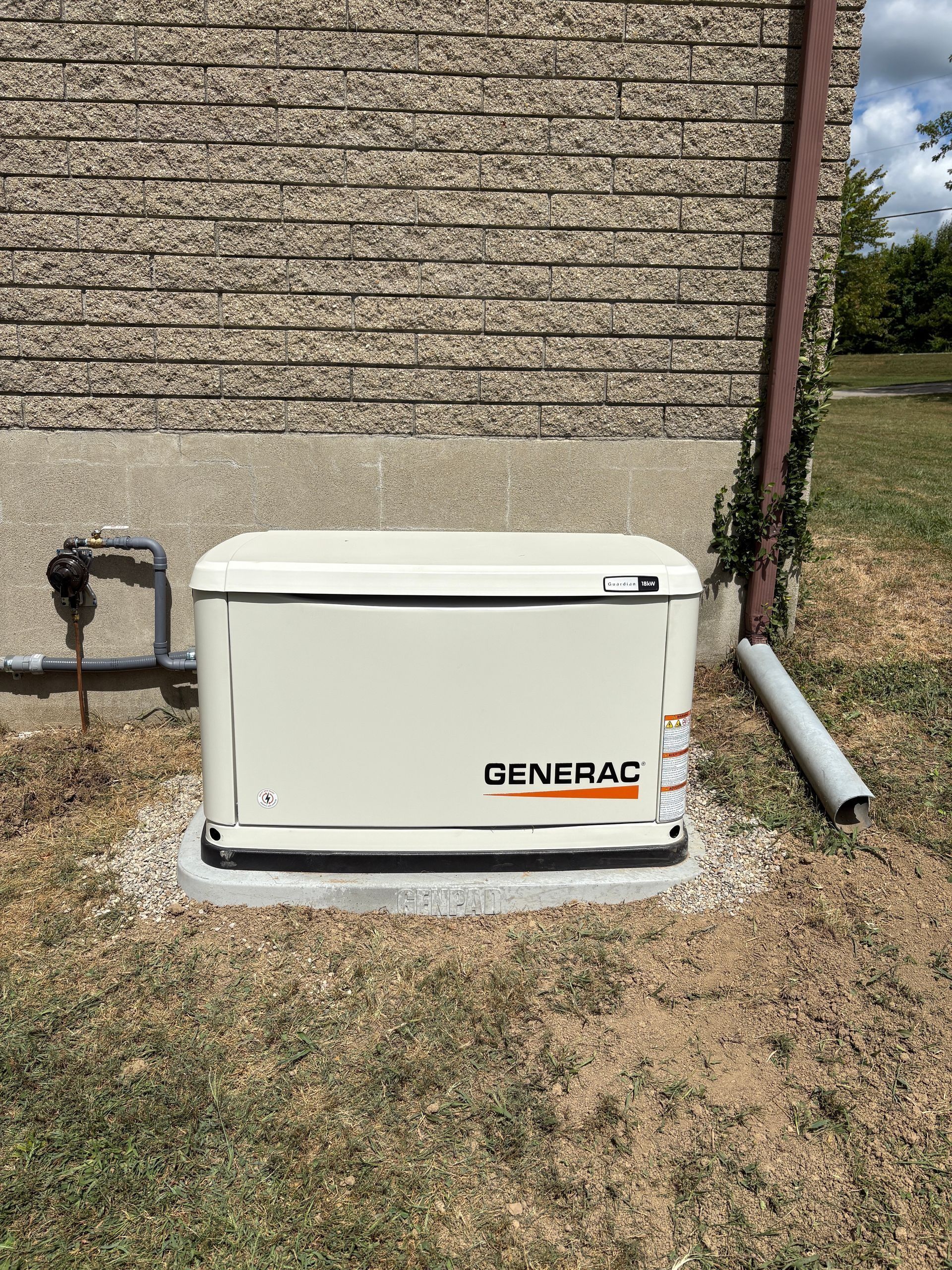 Generac backup generator beside a house wall on a grassy yard with utility pipes nearby