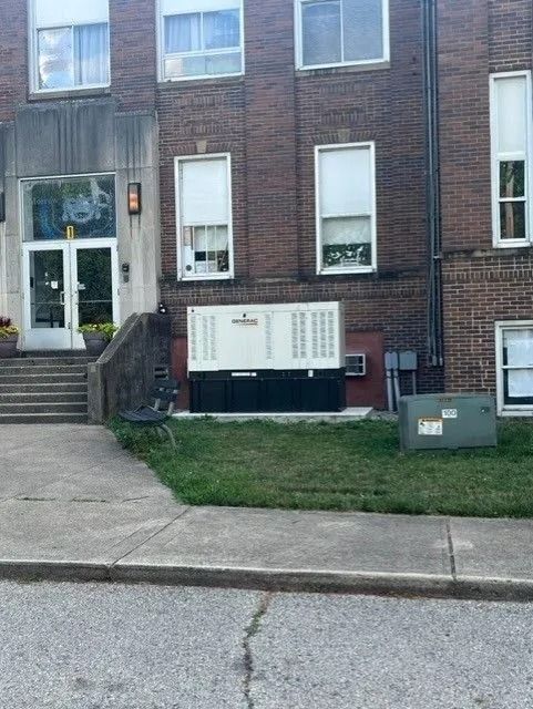 Brick rowhouse with a front stoop, small grass patch, and utility box beside the sidewalk.