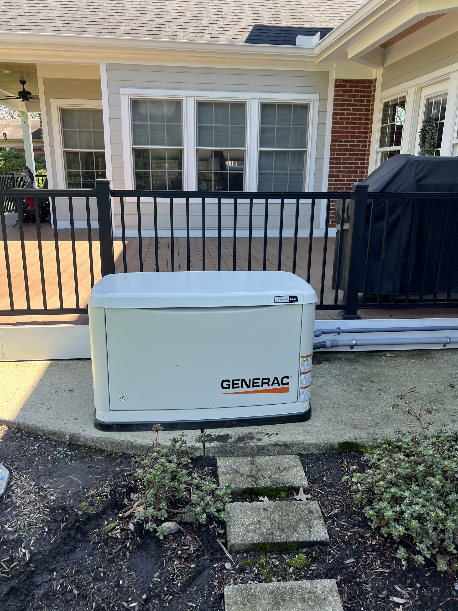 White Generac backup generator beside a house and black fence on a front walkway.
