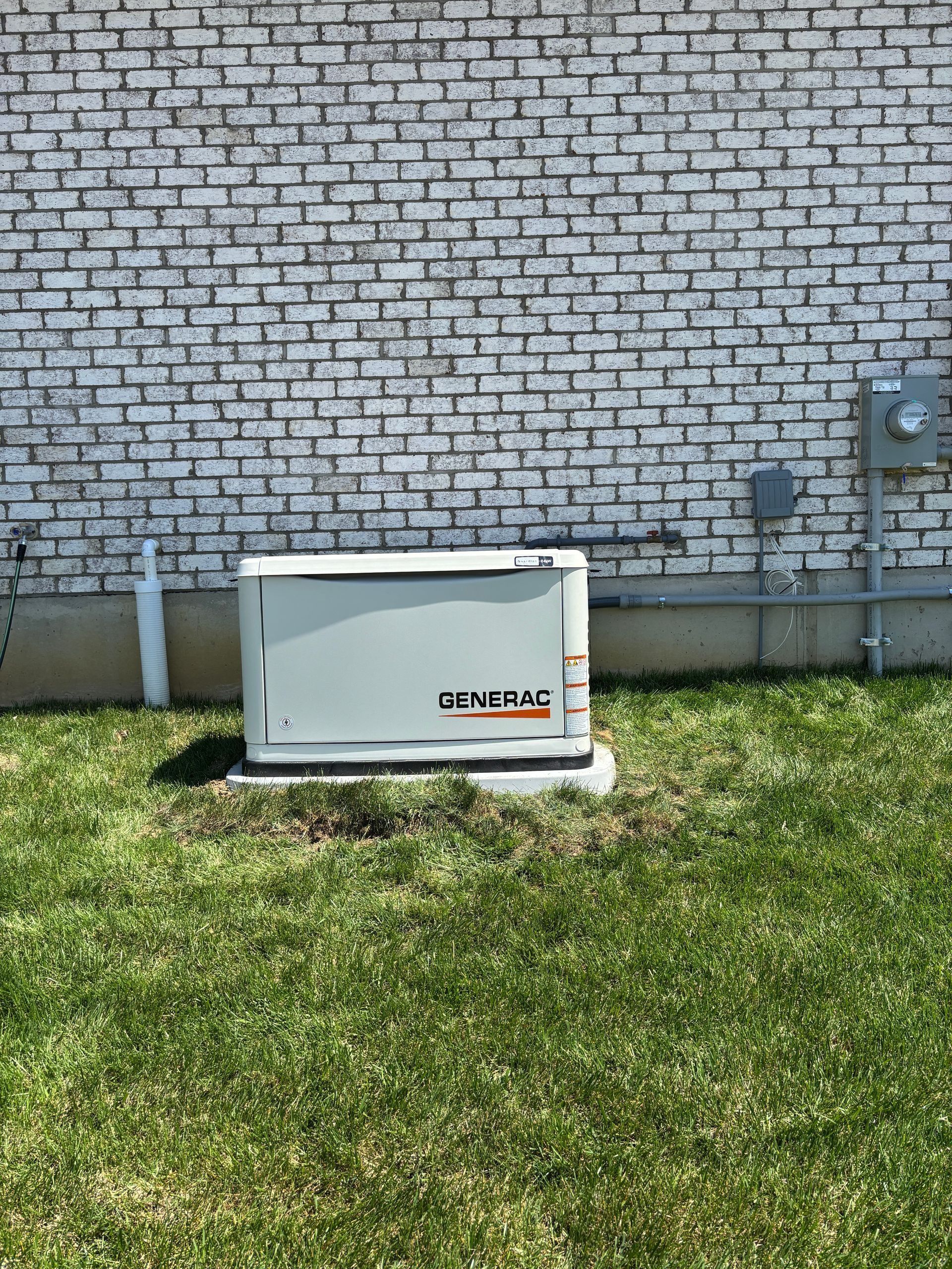 White HVAC unit against a brick wall on a grassy lawn, with utility meter on the right.