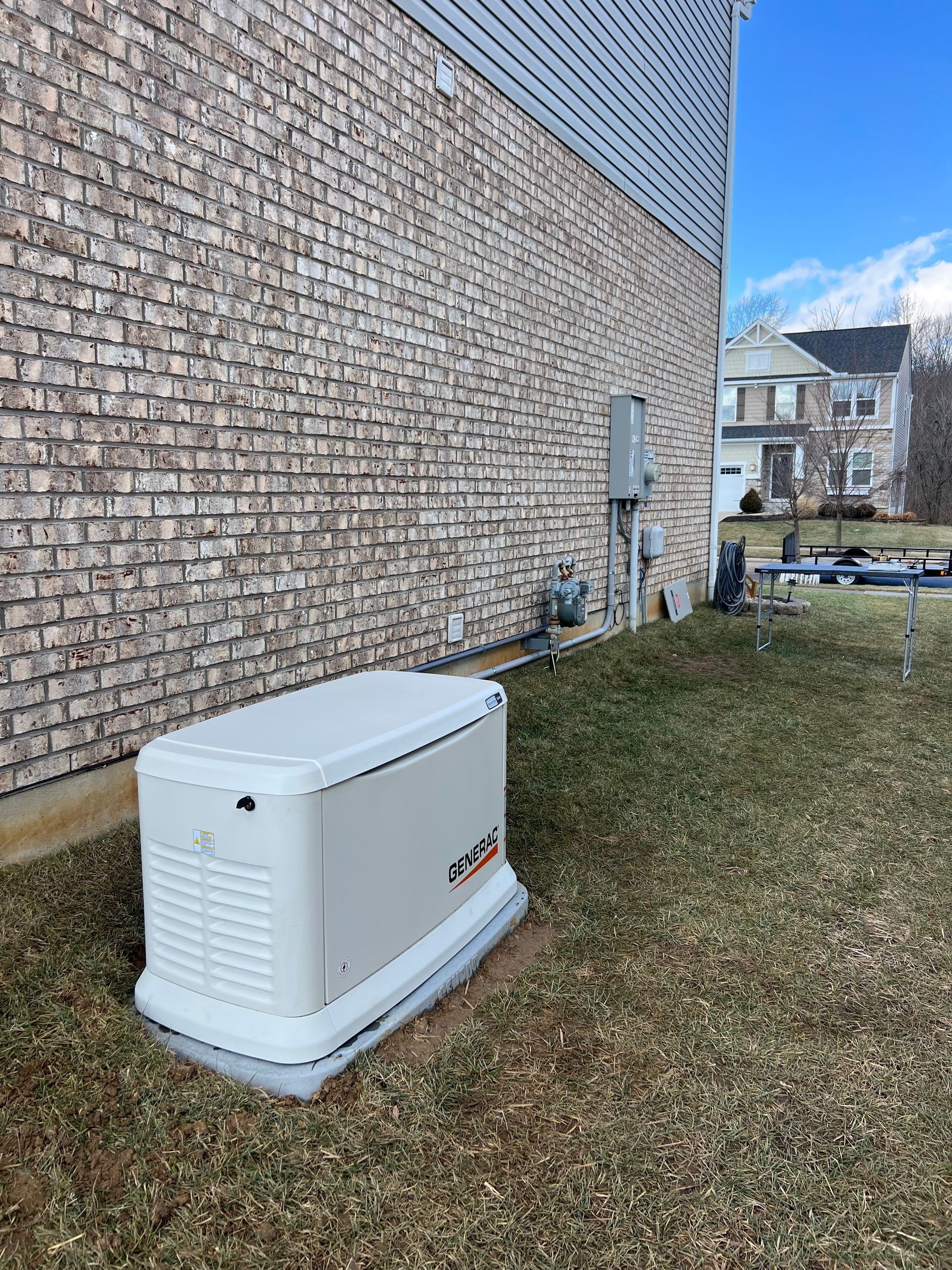 White backup generator beside a brick house on a grassy yard, with a clear blue sky in the background